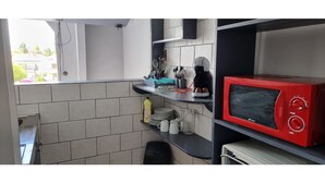 Cocina compacta con microondas rojo, cafetera y varios utensilios de cocina sobre la encimera.