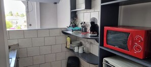 Une cuisine compacte avec un micro-ondes rouge, une machine à café et divers ustensiles de cuisine sur le plan de travail.
