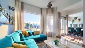 Un soggiorno moderno con un divano color petrolio, un tavolino in legno e vista sul mare.