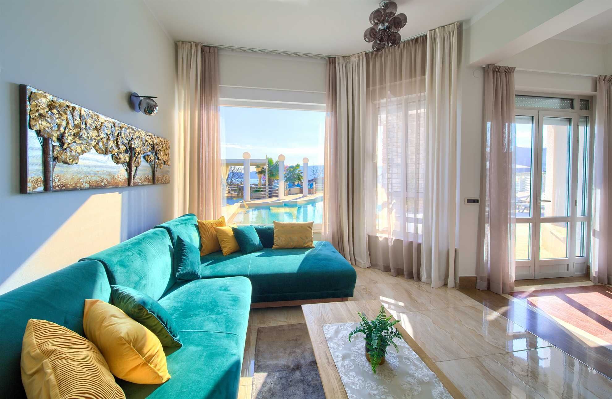 A modern living room with a teal sofa, a coffee table, and a view of a pool and outdoor area.