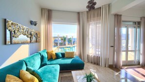 Un soggiorno moderno con un divano color petrolio, un tavolino da caffè e vista su una piscina e area esterna.
