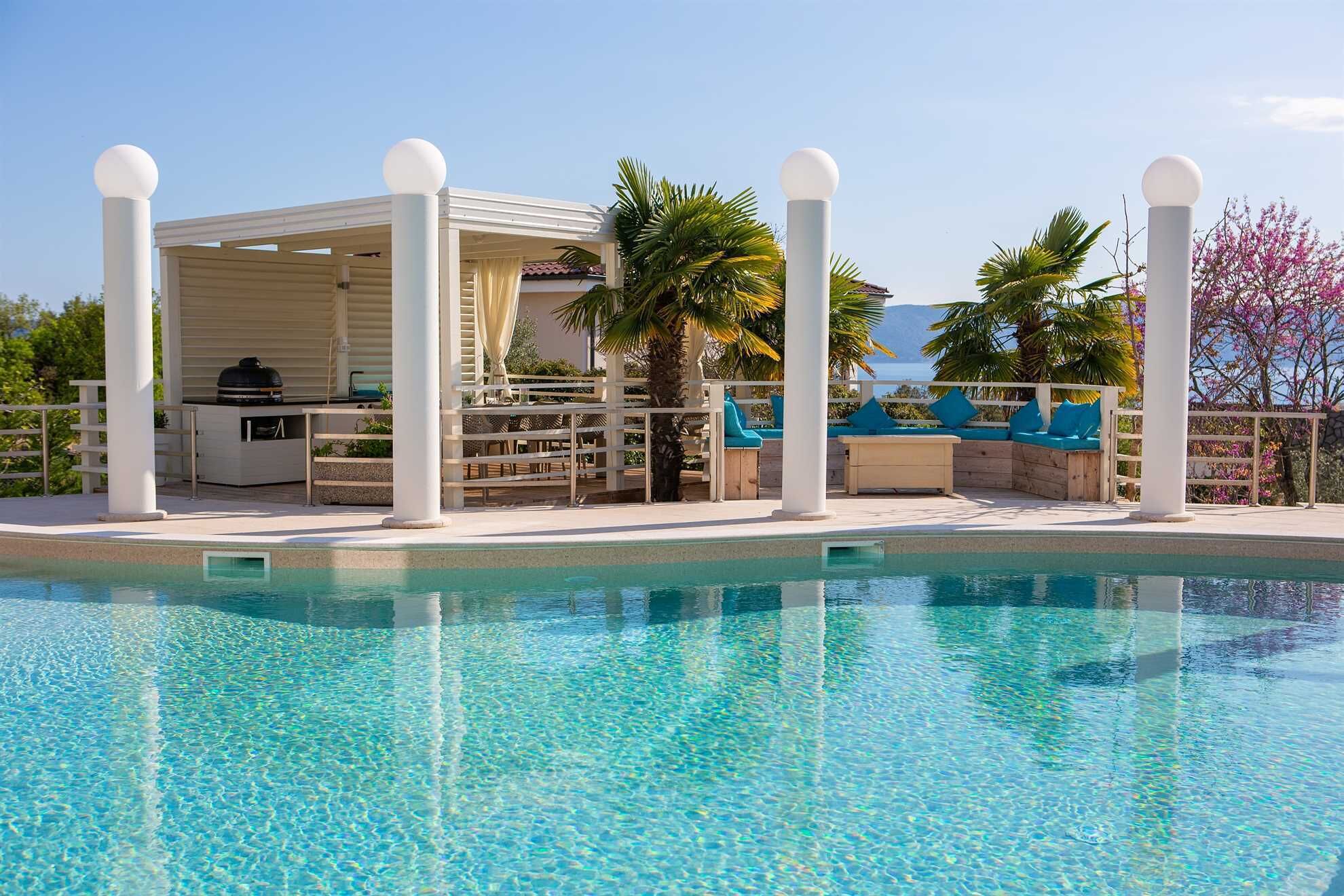 A poolside area with a covered seating area, a grill, and lounge chairs.