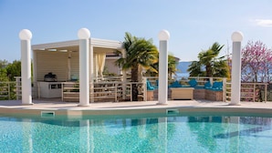 Un'area piscina con un angolo salotto coperto, un barbecue e lettini.