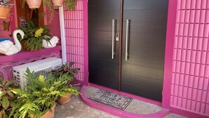 A pink exterior with a black door, potted plants, and a welcome mat.