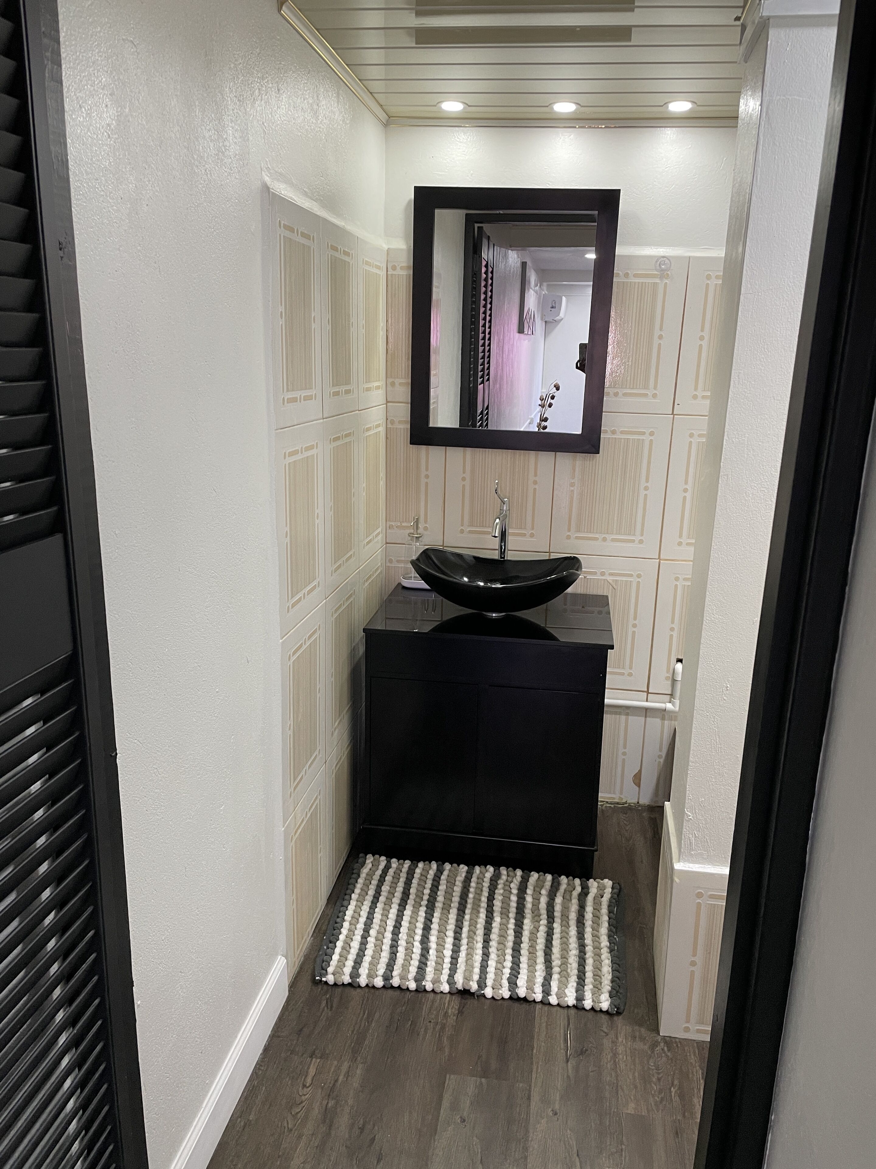 A narrow bathroom with a black sink, a mirror, and a striped rug.