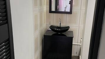 A narrow bathroom with a black sink, a mirror, and a striped rug.