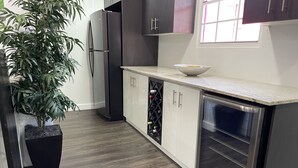 A modern kitchen with dark cabinets, a stainless steel refrigerator, a wine rack, and a built-in oven.