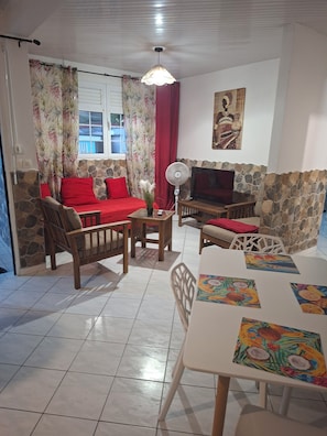 A living room with a sofa, chairs, a table, a fan, and a TV.