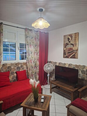 A living room with a sofa, a coffee table, a TV, a fan, and a painting on the wall. - Bright, inviting villa in Anses d'Arlet (Les Anses-d'Arlet)