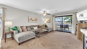 A living room with a sectional sofa, two side tables with lamps, a ceiling fan, and a large window with a view of the outdoors. - 3 Min to Strip! Large Condo, Arcade Game, Pools, Hot tub, Sauna, Golf & Shows! (Branson)
