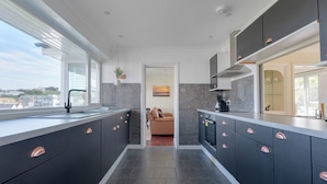A modern kitchen with dark cabinetry, a large island, and a view of the city. - Beach Haven (Wadebridge)