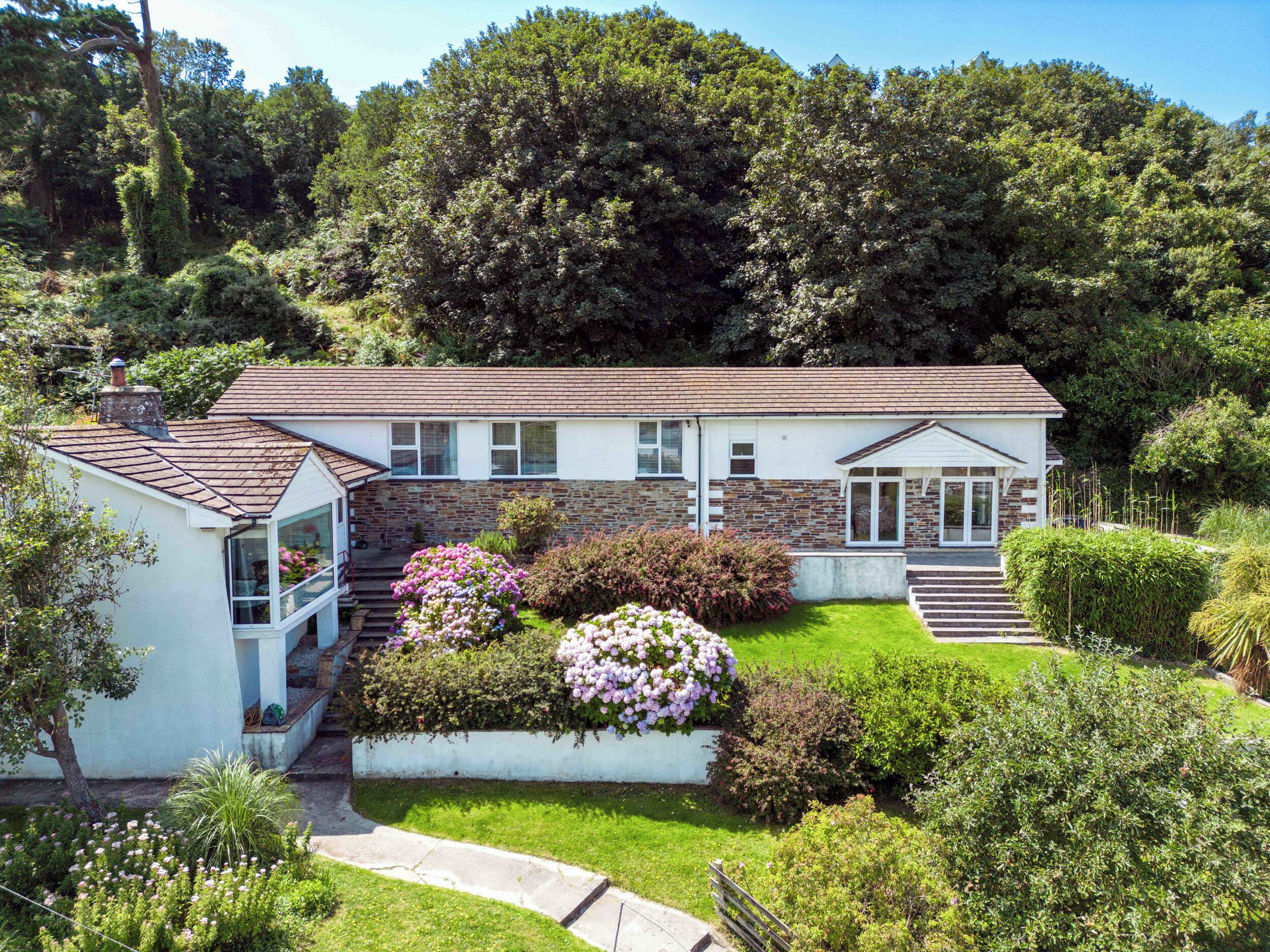 A two-story house with a stone facade, a front porch, and a well-maintained garden with flowering plants.