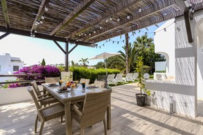An outdoor patio with wicker furniture, a table set with food and drinks, and string lights.