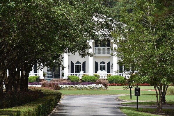 Stately building with a central entrance and arched windows, surrounded by manicured lawns and flowering plants.