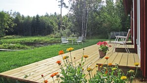Une terrasse en bois avec une zone herbeuse, un petit étang et un bâtiment rouge doté d’un porche.