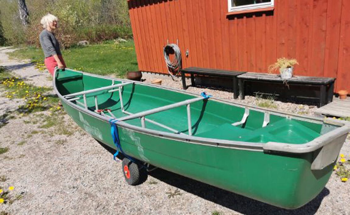 A green boat with a metal frame, a person standing beside it, and a red building in the background.