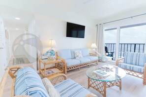 A spacious living area with a sofa, two armchairs, a coffee table, and a TV mounted on the wall.