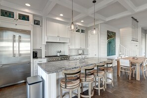 A modern kitchen with white cabinetry, stainless steel appliances, and a central island with bar stools. - The Reel Deal 222 GR (Port Aransas)
