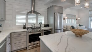 A modern kitchen with stainless steel appliances, white cabinetry, and a marble countertop. - Glass Half Full 205 Fiv-g (Port Aransas)