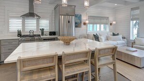 A modern kitchen with a large island, stainless steel appliances, and a dining area with wooden chairs. - Glass Half Full 205 Fiv-g (Port Aransas)