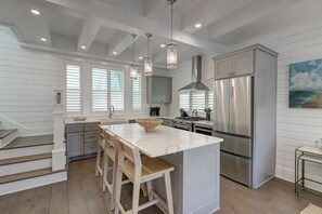 Une cuisine moderne dotée d’un grand îlot central, d’appareils électroménagers en acier inoxydable et de luminaires suspendus.