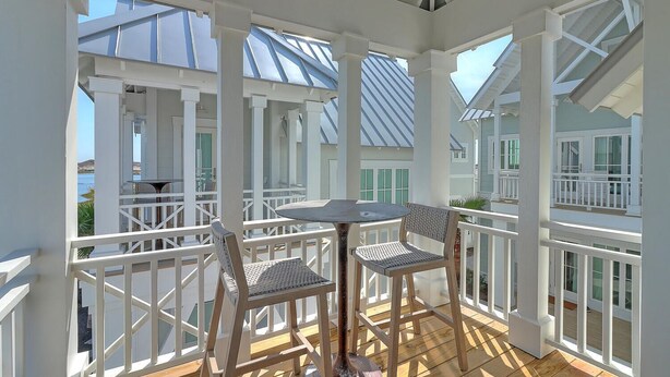 A covered outdoor deck with a table and chairs, white railings, and a view of the sea. - Glass Half Full 205 Fiv-g (Port Aransas)