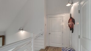 Un pasillo con una puerta blanca, una escalera y una alfombra estampada.
