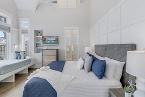 Un dormitorio amplio con una cama grande, una mesita de noche con lámpara, una mesita auxiliar y un estante en la pared con objetos decorativos.