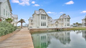 A waterfront property with a wooden deck leading to a calm body of water, surrounded by white buildings with large windows and a symmetrical design. - Edgewater Escape 541 SOU (Port Aransas)