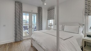 Een slaapkamer met een groot bed, een plafondventilator, een nachtkastje en uitzicht door een glazen deur.