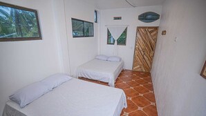 A small, clean room with two beds, a wooden door, and a window with a view of palm trees. - Hotel Pura Natura (Colorado)