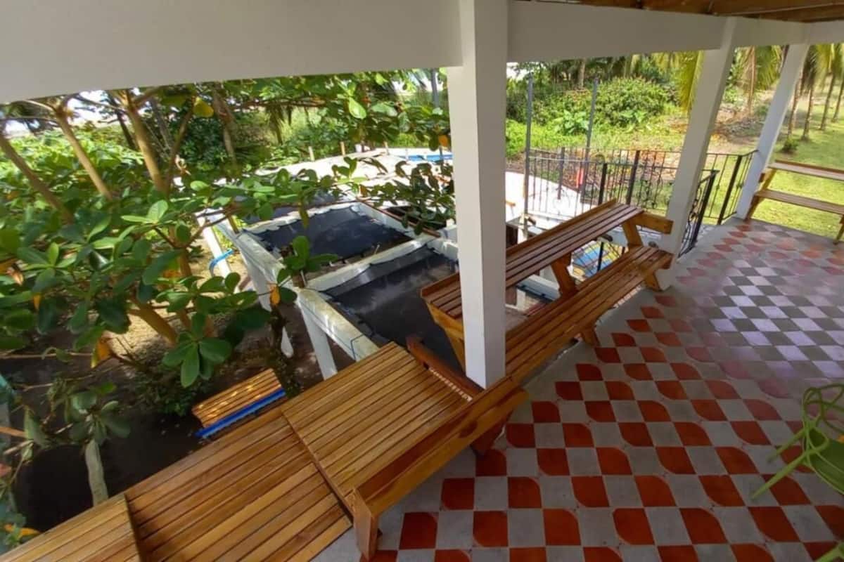 A covered outdoor area with a checkered floor, wooden benches, and a view of a pool and greenery.