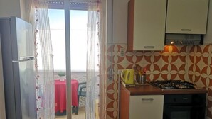 A compact kitchen with a refrigerator, stove, and cabinets. A sliding glass door leads to an outdoor area with a table and chairs. - Appartamento a 100 Metri dal Mare - Tutti i Comfort- Free Wi-fi (Ostuni)