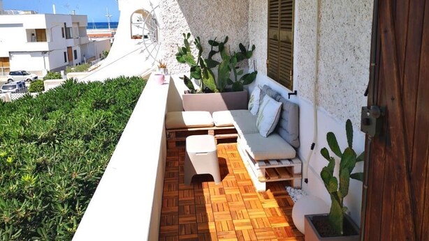 A balcony with a wooden floor, a white sofa, and potted cacti. - Appartamento a 100 Metri dal Mare - Tutti i Comfort- Free Wi-fi (Ostuni)