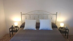 A neatly made bed with white pillows and a dark bedspread, flanked by two bedside tables with lamps and clocks. - Appartamento a 100 Metri dal Mare - Tutti i Comfort- Free Wi-fi (Ostuni)