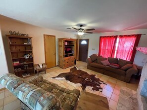 A living room with a sofa, a rug, a wooden cabinet, and a ceiling fan. - Ranchito | Hilltop Cabin w/ Hot Tub & Scenic Views (Hondo)
