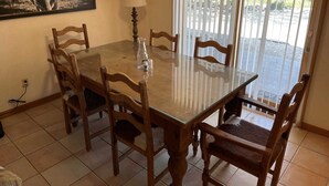 A dining area with a glass table, wooden chairs, a lamp, and a bull painting on the wall. - Ranchito in Hondo Texas (Hondo)