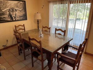 A dining area with a glass-top table, wooden chairs, a lamp, and a painting on the wall. - Ranchito | Hilltop Cabin w/ Hot Tub & Scenic Views (Hondo)