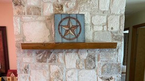 A stone fireplace with a star decoration above it, a wooden mantel, and a bench in front. - Ranchito in Hondo Texas (Hondo)