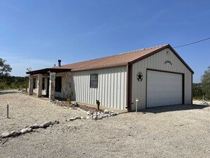 Il s’agit d’un bâtiment d’un seul étage, doté d’un toit en métal et d’une façade blanche. On y trouve une porte de garage et une petite antenne parabolique sur le toit.