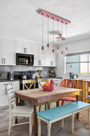 A kitchen with white cabinets, a black microwave, a wooden table, and hanging light fixtures. - Family & Dog Friendly Home | Near Beach | Rockets Launch Views | Pool + Kayaks* (Cocoa Beach)