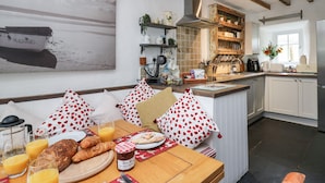 Eine gemütliche Küche mit Holztisch, gedeckt für ein Frühstück, inklusive Croissants, Saft und einem Marmeladenglas.