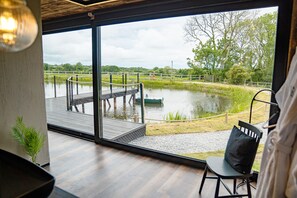 Una habitación con un amplio ventanal que da a una masa de agua, una terraza de madera y una silla.