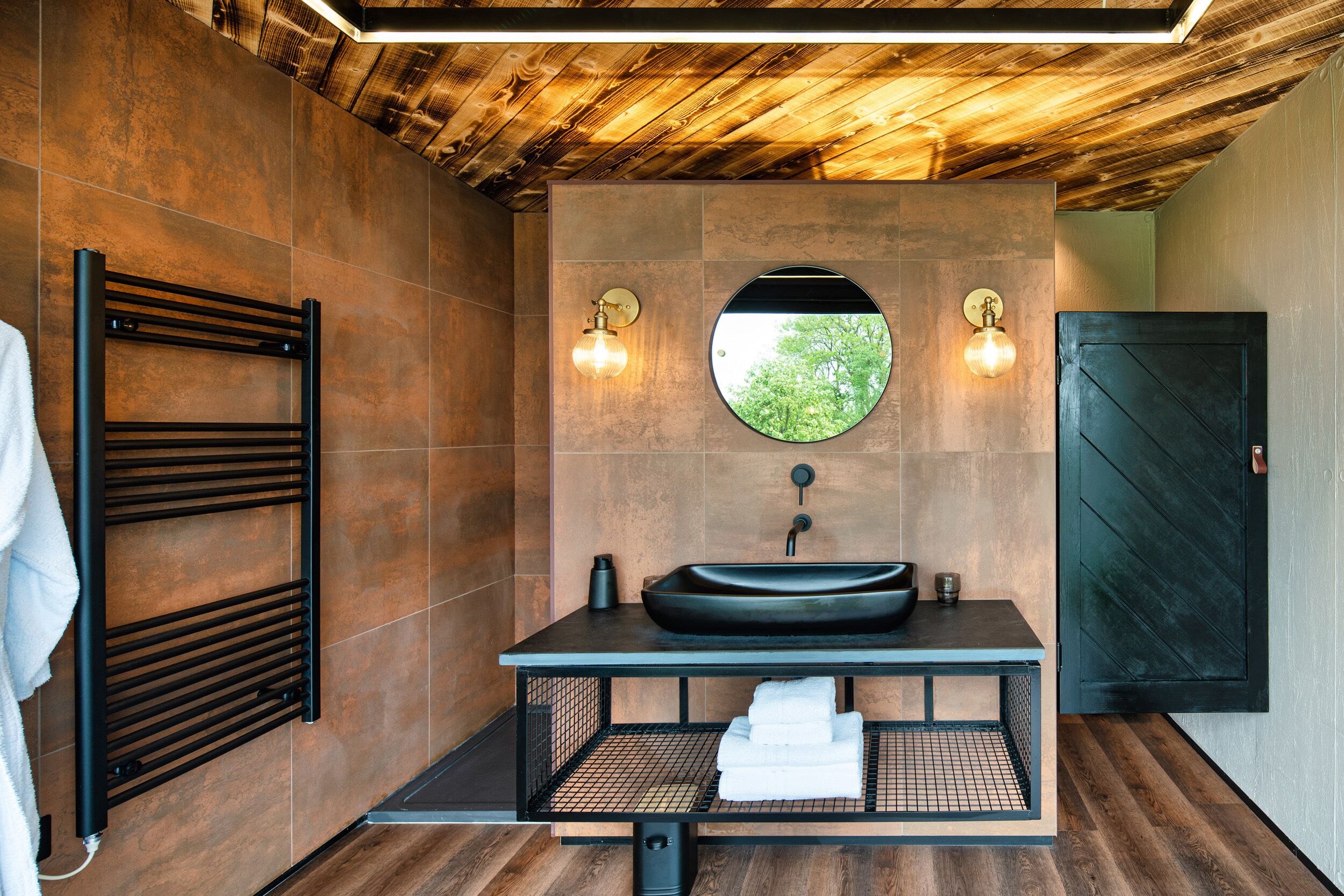 A modern bathroom with a black sink, a towel rack, and a wooden ceiling.