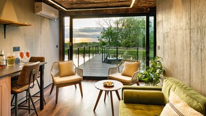 A modern interior with a wooden ceiling, a balcony with a glass railing, and a view of trees and water. - Rusty Boathouse (Llanarth)