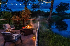 Un patio al aire libre con mobiliario de mimbre, una chimenea y luces colgantes.