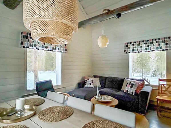 A cozy living room with a sofa, chairs, a dining table, and a hanging light fixture.