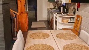 A compact kitchen with white cabinets, a stove, and a microwave. There is a dining table with four woven placemats and two white chairs. - Pajalan piilopirtti by Interhome (Kuusamo)