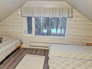 Quarto de dormitório com duas camas, uma janela com vista para árvores e um radiador.