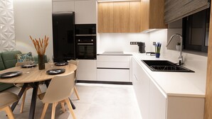 Eine moderne Küche mit weißen Schränken, einem eingebauten Backofen, einer schwarzen Dunstabzugshaube und einer Spüle aus Edelstahl.